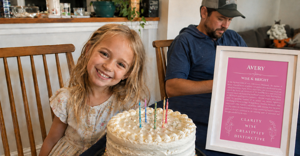 Smiling child beside a birthday cake and a framed personalized name meaning print